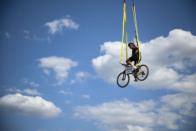 A spectator sits atop a bicycle suspended above the race route during the 16th stage of the 111th edition of the Tour de France cycling race, 188,6 km between Gruissan and Nimes, southern France, on July 16, 2024. (Photo by Marco Bertorello/AFP Photo)