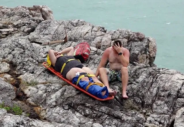 In this May 26, 2016 photo taken from video, rescued tourists rest on the shore after their boat capsized on Koh Samui, Thailand. Officials say a speed boat carrying 32 tourists and four crew members to the tourist resort island of Koh Samui capsized, leaving two foreigners dead and two others missing. (Photo by AP Photo)