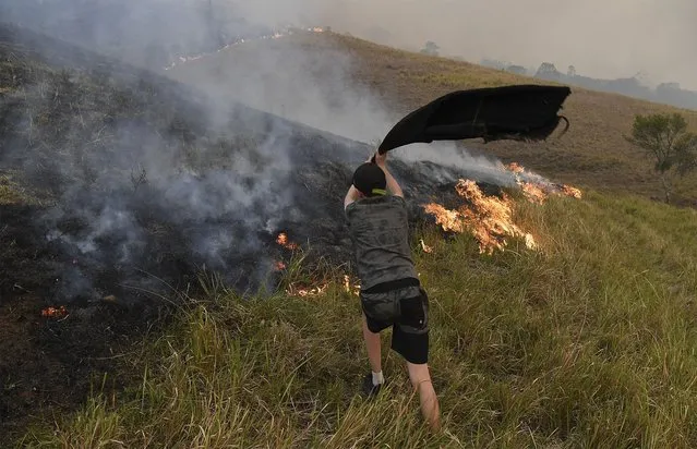 A boy uses a towel to help put out flames as they encroach on farmland near the town of Taree, some 350kms north of Sydney, on November 14, 2019. The death toll from devastating bushfires in eastern Australia has risen to four after a man's body was discovered in a scorched area of bushland, police said on November 14. (Photo by William West/AFP Photo)
