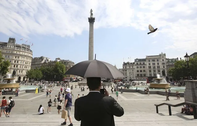 A man takes a photograph under the shade of an umbrella in Trafalgar Square in London, Britain July 1, 2015. (Photo by Paul Hackett/Reuters)