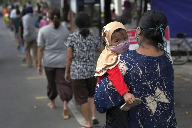 A woman carries her daughter as they queue up for free iftar, the evening meal with which Muslims end their daily Ramadan fast at sunset, distributed for the needy in Jakarta, Indonesia, Monday, April 18, 2022. Muslims in many parts of the world are observing Ramadan, the holiest month in Islamic calendar, where they refrain from eating, drinking, smoking, and s*x from dawn to dusk. (Photo by Dita Alangkara/AP Photo)