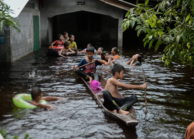 Children ride on a boat outside a house affected by floodwaters following heavy rains Sungai Kolok district in southern Thai province of Narathiwat on December 2, 2019. (Photo by Madaree Tohlala/AFP Photo)