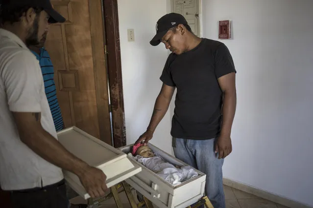 Fernando Gonzalez touches the head of his daughter Anabella as he looks at her body one last time in Maracaibo, Venezuela, November 27, 2019. Gonzalez said doctors told him his 11-month-old died of malnutrition, however, “Sepsis. Central nervous system infection” was written on her death certificate. The father said he was thankful his boss at the cemetery donated his daughter's wake and cremation services, because he didn't have the money for a funeral. (Photo by Rodrigo Abd/AP Photo)