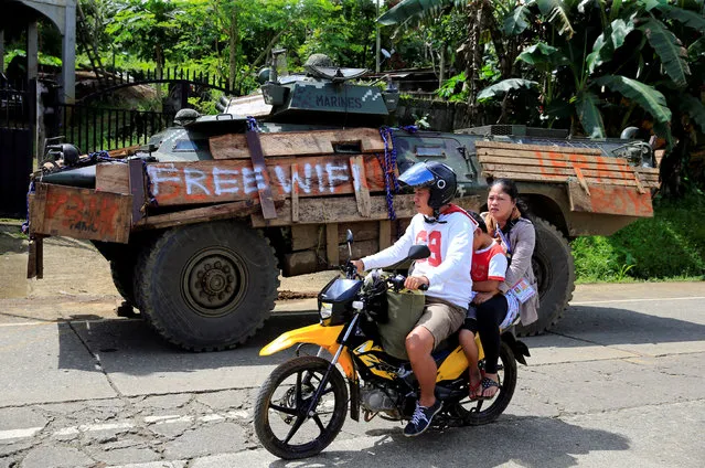 People on a motorcycle ride past an armoured personnel carrier parked along a main road in Pantar village, Lanao Del Norte, Philippines June 21, 2017. (Photo by Romeo Ranoco/Reuters)