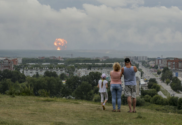 In this photo taken on Monday, August 5, 2019, a family watches explosions at a military ammunition depot near the city of Achinsk in eastern Siberia's Krasnoyarsk region, in Achinsk, Russia. Russian officials say powerful explosions at a military depot in Siberia left 12 people injured and one missing and forced over 16,500 people to leave their homes. (Photo by Dmitry Dub/AP Photo)