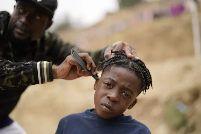 Wiggins Nordelus, of Haiti, left, cuts his son Samuel's hair outside of a shelter for migrants, Monday, May 23, 2022, in Tijuana, Mexico. Nordelus waits in Mexico as he hopes to apply for asylum in the United States. A federal judge in Louisiana blocked the Biden administration from lifting a public health order used to quickly return migrants at the southern border, including asylum-seekers. (Photo by Gregory Bull/AP Photo)