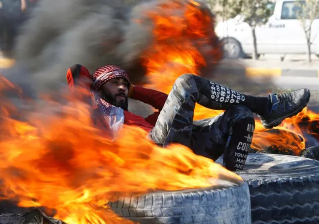 An Iraqi demonstrator sits amid burning tires blocking a road during ongoing anti-government protests in Najaf, Iraq on February 2, 2020. (Photo by Alaa al-Marjani/Reuters)