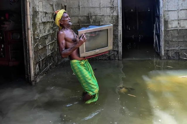 A man carries his belongins from his partially submerged house at Barsimolua village in Nalbari district, in India's Assam state on June 24, 2022. (Photo by Biju Boro/AFP Photo)