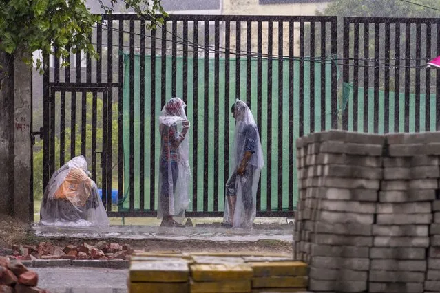 People stand covered in plastic sheets as it rains in New Delhi Thursday, June 30, 2025. India's monsoon season runs from June to September. (Photo by Rajesh Kumar Singh/AP Photo)