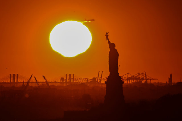 An airplane flies overhead as the sun sets behind the Statue of Liberty in New York on November 12, 2024. (Photo by Angela Weiss/AFP Photo) 