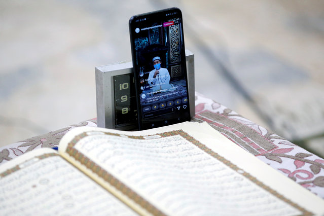 Bambang Suprianto, an Imam wearing a protective mask, is seen in the screen of a smartphone as he reads the Koran while streamed through social media inside Sunda Kelapa mosque, closed as the government imposed large-scale restrictions to prevent the spread of coronavirus disease (COVID-19), a moment before iftar during the holy fasting month of Ramadan, in Jakarta, Indonesia, April 25, 2020. (Photo by Willy Kurniawan/Reuters)