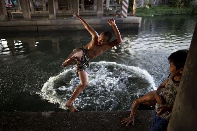 Thai children joyfully jump into a canal under an expressway in Bangkok, Thailand, Tuesday, May 12, 2020. Thai government continue to ease restrictions in capital Bangkok that were imposed weeks ago to combat the spread of COVID-19. (Photo by Gemunu Amarasinghe/AP Photo)