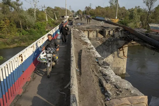 A man drives by motorbike on a destroyed bridge across Oskil river during evacuation in recently liberated town Kupiansk, Ukraine, Saturday, October 1, 2022. (Photo by Evgeniy Maloletka/AP Photo)