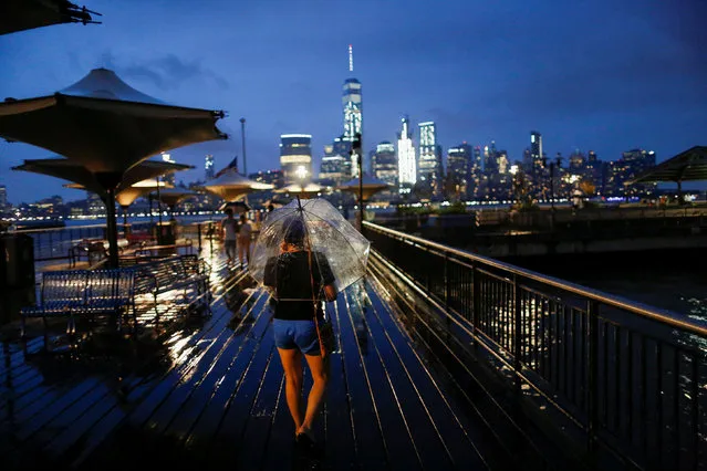 A woman walks through a park along the Hudson River across from New York's Lower Manhattan and One World Trade Center as rain falls in Exchange Place, New Jersey, U.S., July 30, 2016. (Photo by Eduardo Munoz/Reuters)