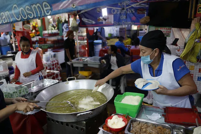 Sabina Hernandez Bautista, 59, prepares food in a stall inside Mercado San Cosme, where some vendors have put in place their own protective measures against coronavirus while others continue to work without masks or barriers, in Mexico City, Thursday, June 25, 2020. “We are all afraid”, said Bautista, who added she had no choice but to work to be able to feed her family, including her daughter who is attending university. (Photo by Rebecca Blackwell/AP Photo)