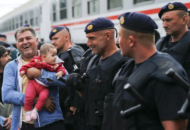 A migrant laughs as he holds a baby beside police at the train station in Tovarnik, Croatia, September 20, 2015. (Photo by Antonio Bronic/Reuters)