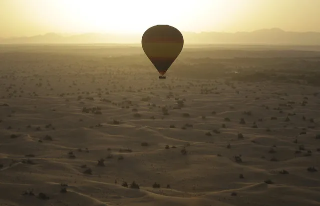 The sun rises from behind the Hajjar Mountains as one of the world largest hot air balloons carries 24 passengers flying over the Margham desert about 60 km (37 miles) southeast of Dubai, United Arab Emirates, Tuesday, October 21, 2014. (Photo by Kamran Jebreili/AP Photo)