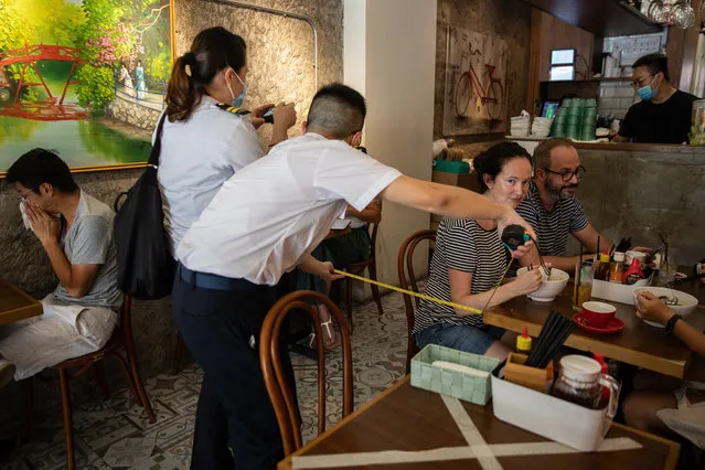 Officers with the Food and Environmental Hygiene Department measure the distance between tables in a restaurant in Hong Kong, China, 16 July 2020. According to guidelines by the government, tables within any catering premises must be arranged in a way to ensure there is a distance of at least 1.5 metres between one table and another table at the premises. Hong Kong Health authorities have been reporting dozens of local coronavirus disease (COVID-19) cases daily over the last four days. (Photo by Jerome Favre/EPA/EFE)