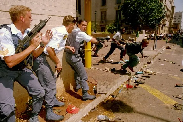 Police take cover as Zulu Inkatha Freedom Party (IFP) supporters flee as they are fired upon by unidentified gunmen, March 28, 1994, in Johannesburg. South Africa is engrossed in debate over the legacy of apartheid's last president, F.W. de Klerk, who died at 85 and is to be buried Sunday, Nov 21, 2021. Some people want to remember de Klerk as the liberator of Nelson Mandela, but others say he was responsible for racist murders. (Photo by Peter Dejong/AP Photo/File)