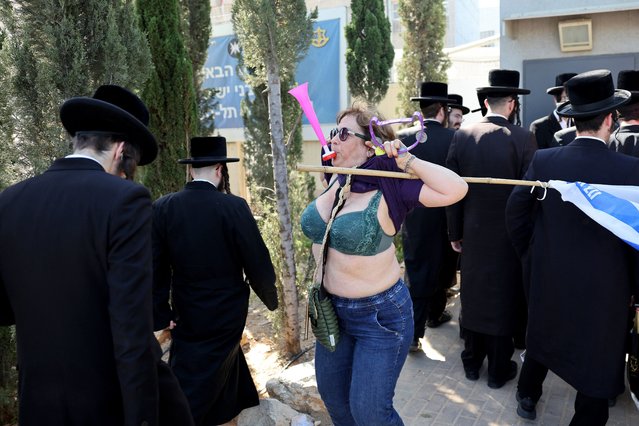 An Israeli protester lifts her T-shirt next to Ultra-Orthodox Jewish men outside an army recruiting office in the town of Kiryat Ono near Tel Aviv on March 5, 2024, during a demonstration against their exemption from serving in the army. Since the October 7 attack by Palestinian militants, the question surrounding whether the insular community, whose members see army service as conflicting with their religious duties, should be obligated to serve has sparked debate and led to protests against their decades-long exemptions. (Photo by Jack Guez/AFP Photo)