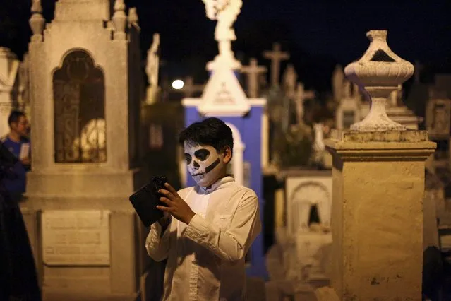 A child, with his face painted as a skull, uses his cellphone while waiting for the traditional parade called "Paseo de las Animas", or Parade of Souls, as part of Day of the Dead celebrations in Merida, Mexico, October 31, 2015. (Photo by Lorenzo Hernandez/Reuters)