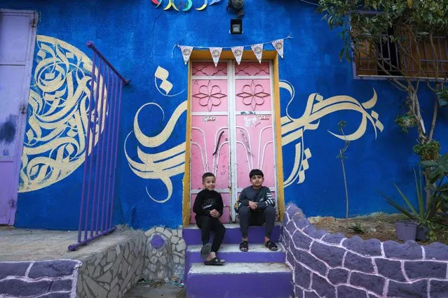 Children sit at the doorstep of a house, painted in vivid colours as part of an initiative by a Palestinian artist, in the Zeitun district of Gaza City, on March 12, 2023. (Photo by Mahmud Hams/AFP Photo)