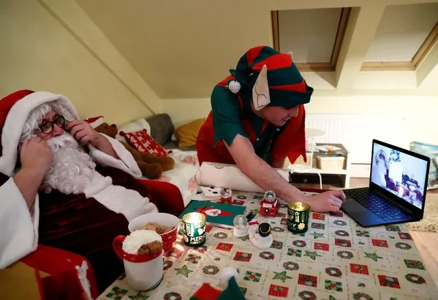 An assistant helps Pal Pillmayer, dressed as Santa Claus, as he prepares to interact with children by video chat, amid the coronavirus disease (COVID-19) outbreak in Budapest, Hungary, November 30, 2020. (Photo by Bernadett Szabo/Reuters)