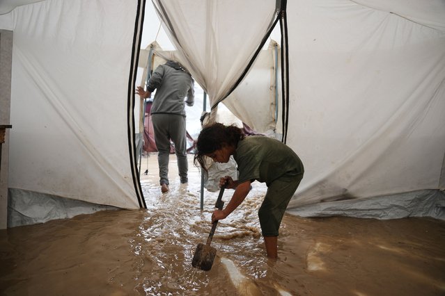 Saja Fayyad, 7, tries to clear water from her family's flooded tent at a temporary camp for displaced Palestinians after heavy rainfall in Deir al-Balah, central Gaza Strip, Tuesday, November 25, 2025. (Photo by Abdel Kareem Hana/AP Photo)