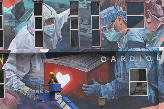 A worker adds finishing touches to giant mural tribute to frontline workers in the COVID-19 coronavirus pandemic outside a hospital in Kuala Lumpur, Malaysia, on Thursday, January 21, 2021. Malaysian Prime Minister Muhyiddin Yassin has unveiled a new 15 billion ringgit ($3.7 billion) stimulus to bolster consumption, with the economy expected to reel from a second coronavirus lockdown and an emergency declaration. (Photo by Vincent Thian/AP Photo)