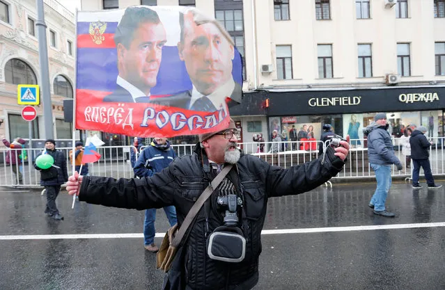 A man holds a Russian flag with images of Russian President Vladimir Putin and Prime Minister Dmitry Medvedev, as he takes a selfie during a demonstration on National Unity Day in central Moscow, Russia, November 4, 2016. (Photo by Maxim Zmeyev/Reuters)