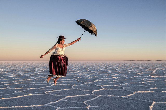 A young cholita from “Warmi Empollerada” project is portrayed emulating to fly with an umbrella during the sunset at the Salar de Uyuni (Uyuni Salt Flats), southwestern Bolivia, on June 25, 2023. The Salar de Uyuni is the world's largest salt flat and a top tourist destination in Bolivia and South America. (Photo by Marcelo Perez Del Carpio/Anadolu Agency via Getty Images)