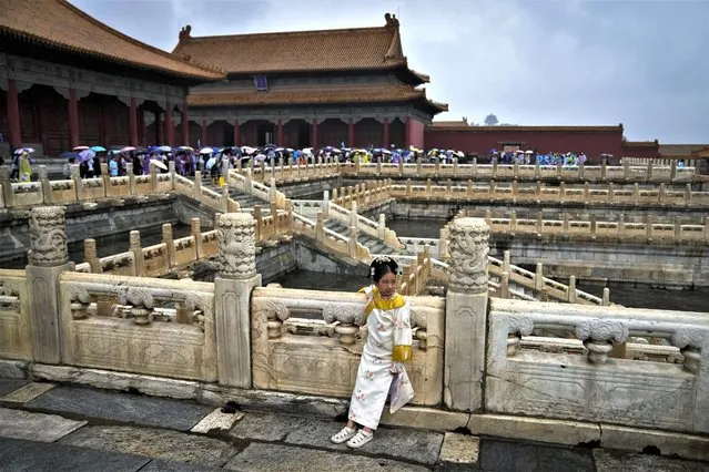 A girl wearing a traditional costume stands as visitors carrying umbrellas tour the Forbidden City on a rainy day in Beijing, Thursday, July 13, 2023. (Photo by Andy Wong/AP Photo)