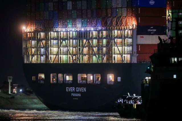 This picture taken late on March 27, 2021 shows a view of a tugboat by the Panama-flagged MV “Ever Given” (owned by Taiwan-based Evergreen Marine) container ship, which has been wedged diagonally across the span of the canal about six kilometres north of the Suez Canal's entrance by the Red Sea port city of Suez since March 23, blocking the waterway in both directions. (Photo by Ahmed Hasan/AFP Photo)