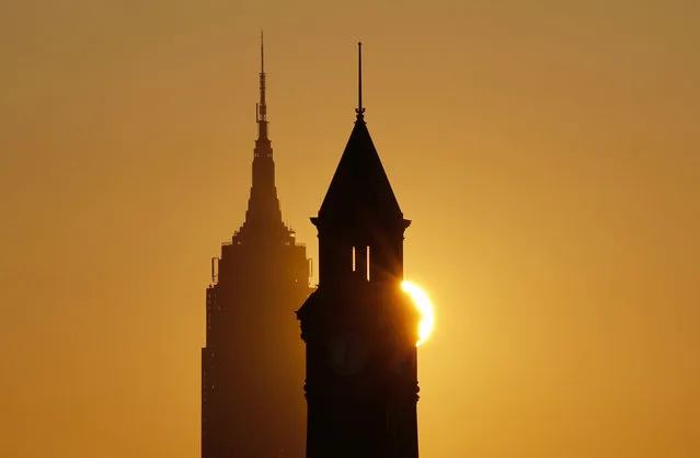 The sun rises behind the Empire State Building in New York City and the Lackwanna clock tower in Hoboken, New Jersey on May 15, 2023, as seen from Jersey City, New Jersey. (Photo by Gary Hershorn/Getty Images)