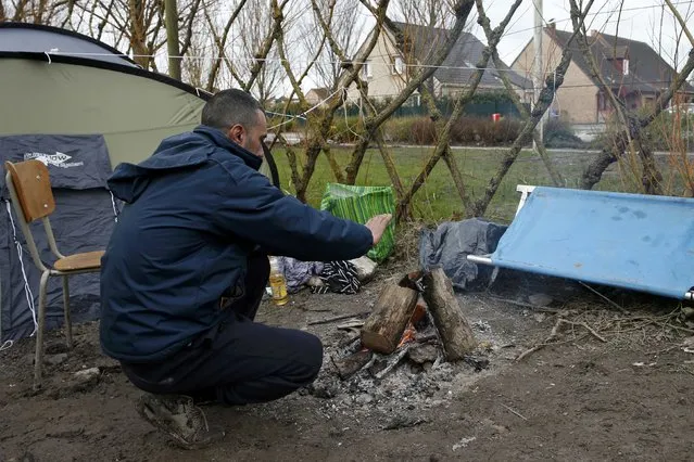 A migrants warms himself by a fire outside his shelter located in a field called the Grande-Synthe jungle, near Dunkirk, northern France, January 12, 2016. (Photo by Benoit Tessier/Reuters)