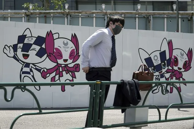 A man wearing a protective mask to help curb the spread of the coronavirus stands near drawings of Miraitowa and Someity, official mascots for the Tokyo 2020 Olympics and Paralympics, on a construction wall Tuesday, April 20, 2021, in Tokyo. (Photo by Eugene Hoshiko/AP Photo)