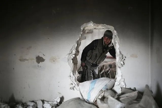 A fighter from Jaish al-Islam (Islam Army), the foremost rebel group in Damascus province who fiercely oppose to both the regime and the Islamic State group, walks through a hole in the wall in Harasta Qantara, near Marj al-Sultan on the eastern outskirts of Damascus, on January 23, 2016, during clashes with government forces after they infiltrated into the government-held area. (Photo by Amer Almohibany/AFP Photo)