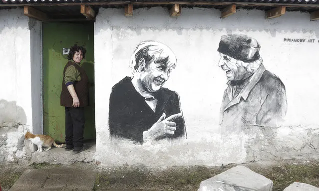 Ivanka Toneva enters her house yard, next to the mural depicting her husband Krustyo Tonev, and German chancellor Angela Merkel, in the Bulgarian village of Staro Zhelezare on Wednesday, January 27, 2016. The sleepy village of Staro Zhelezare in central Bulgaria is harnessing the power of celebrities, hoping for an economic revival through art. (Photo by Valentina Petrova/AP Photo)
