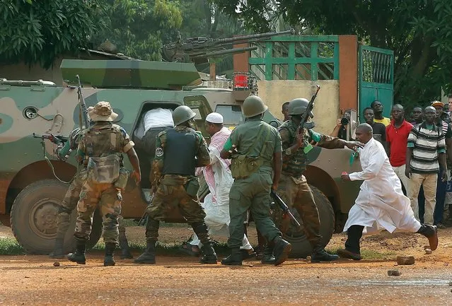 FOMAC troops , regional peacekeepers, evacuate Muslim clerics under a hail of fire from the St Jacques Church in Bangui, Central African Republic, Thursday December 12, 2013. An angry crowd had gathered outside the church following rumors that a Seleka general was inside. More than 500 people have been killed over the past week in sectarian fighting in Central African Republic. (Photo by Jerome Delay/AP Photo)