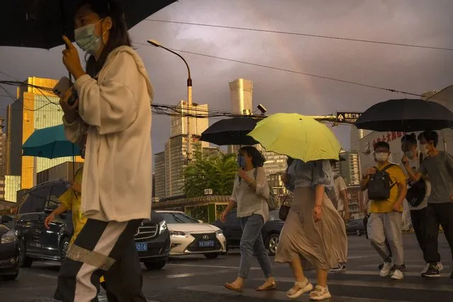 People wearing face masks to protect against COVID-19 walk across an intersection as a rainbow forms in the sky during the evening rush hour in Beijing, Thursday, August 26, 2021. (Photo by Mark Schiefelbein/AP Photo)