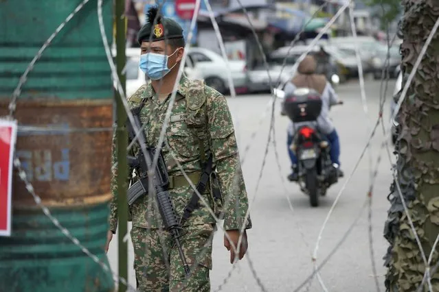 A soldier stands guard near barbwire at Kerinchi area placed under the enhanced movement control order (EMCO) due to drastic increase in the number of COVID-19 cases recorded in Kuala Lumpur, Malaysia, Sunday, July 4, 2021. Malaysia starts further tightening movement curbs and imposes a curfew in most areas in its richest state Selangor and parts of Kuala Lumpur, where coronavirus cases remain high despite a national lockdown last month. (Photo by Vincent Thian/AP Photo)