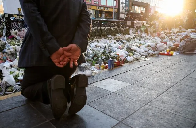 A mourner kneels next to floral tributes near the site of a crowd crush that happened during Halloween festivities, in Seoul, South Korea on November 2, 2022. (Photo by Kim Hong-Ji/Reuters)