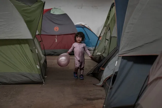A girl holds a balloon as she walks among tents inside an empty warehouse used as a shelter set up for migrants in downtown Tijuana, Mexico, Wednesday, January 2, 2019. Discouraged by the long wait to apply for asylum through official ports of entry, many migrants from recent caravans are choosing to cross the U.S. border wall and hand themselves in to border patrol agents. (Photo by Daniel Ochoa de Olza/AP Photo)