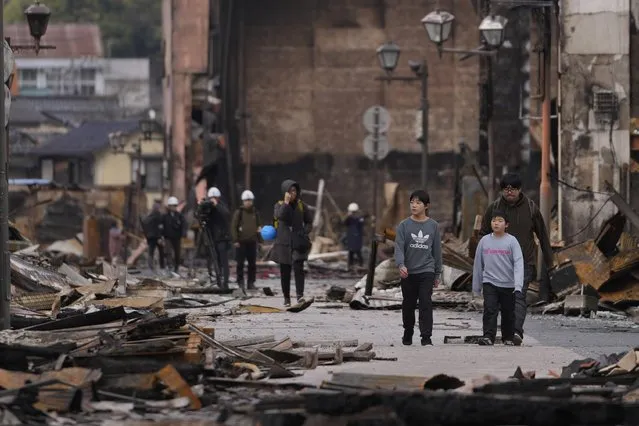 People walk through debris after a fire at a shopping area in Wajima in the Noto peninsula, facing the Sea of Japan, northwest of Tokyo, Friday, January 5, 2024, following Monday's deadly earthquake. (Photo by Hiro Komae/AP Photo)
