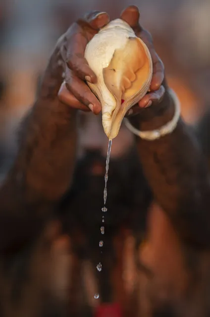 In this Tuesday, January 15, 2019 photo, a sadhu, a Hindu holy man, pours water from a shell as he takes a ceremonial cleansing dip at Sangam, the confluence of the rivers Ganges, Yamuna and mythical Saraswati, during the Kumbh Mela festival in Prayagraj, India. (Photo by Bernat Armangue/AP Photo)