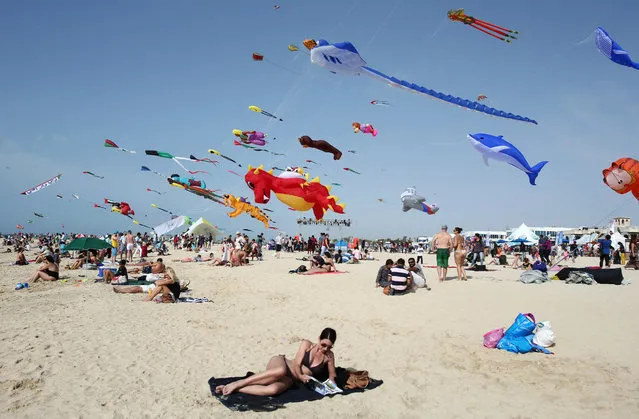 A woman enjoys the sun as hundreds of kites from around the world fly through the sky at the Jumeirah beach during an international kite festival in Dubai, United Arab Emirates, Saturday, March 19, 2016. (Photo by Kamran Jebreili/AP Photo)