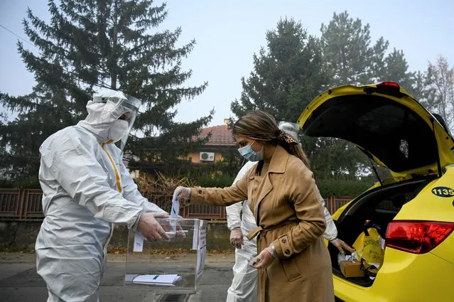 An electoral staff member of a mobile polling center, wearing Personal Protective Equipment (PPE), presents a ballot box to a woman in self-quarantine to collect her vote for the second-round of the presidential election and the parliamentary elections in the village of Voluek on November 21, 2021. Bulgarians vote on November 21, 2021 to elect their president, a largely ceremonial role that the current incumbent has transformed and put at the heart of the struggle against corruption in the EU's poorest country. (Photo by Nikolay Doychinov/AFP Photo)