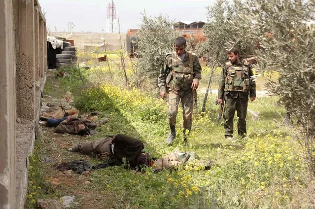 Syrian army soldiers loyal to Syria's President Bashar al-Assad inspect a dead body, which according to them was a member of the “Free Syrian Army”, in al-Maamel area in Aleppo's countryside, after claiming to have advanced and regained control of it, on March 24, 2014. (Photo by Jorge Ourfalian/Reuters)