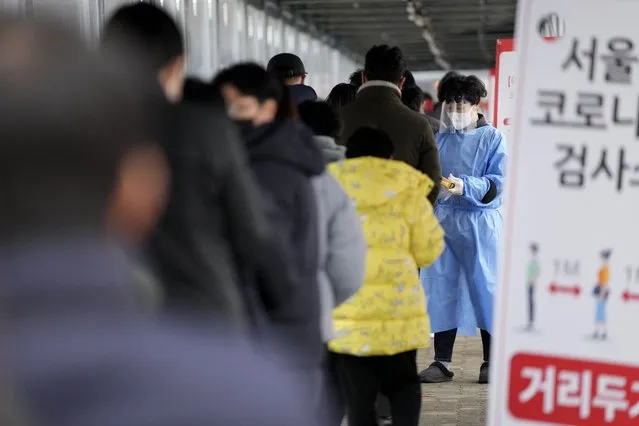 A health worker wearing protective gear holds plastic gloves for visitors at a temporary screening clinic for the coronavirus in Seoul, South Korea, Tuesday, January 25, 2022. South Korea recorded more than 8,000 new coronavirus infections for the first time Tuesday as health authorities reshape the country's pandemic response to address a surge driven by the highly contagious omicron variant. (Photo by Lee Jin-man/AP Photo)