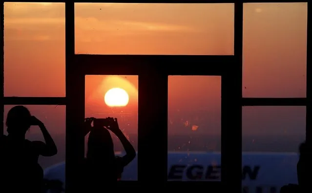 Tourist photograph the sunrise at the airport terminal on the Greek island of Santorini, Greece, July 1, 2015. (Photo by Cathal McNaughton/Reuters)